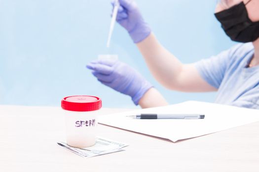 a jar with a red cap with sperm, stand on a banknote of 500 euros, a sperm donor concept, female hands with a pipette and a jar for analysis in the background in blue gloves, blue background, copy space, paper and pen on the table