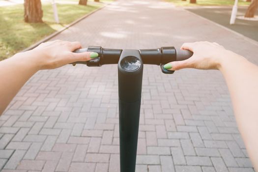 Active woman riding an electric scooter on path outdoor, point of view in first person. Concept of eco transport.