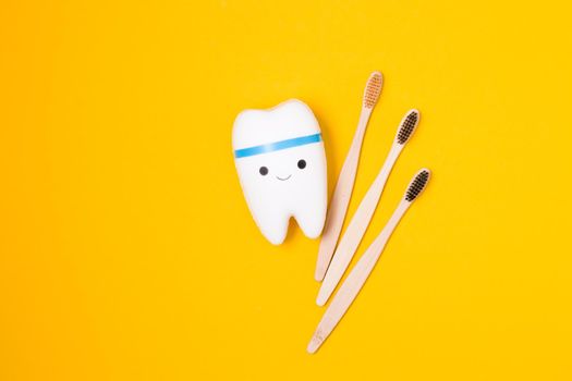smiling tooth model and bamboo toothbrushes on yellow background, happy tooth, white healthy tooth, copy space, oral care concept