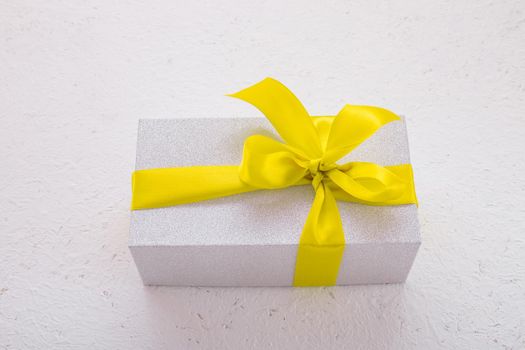 shiny gift box with yellow ribbon on white background top view copy space