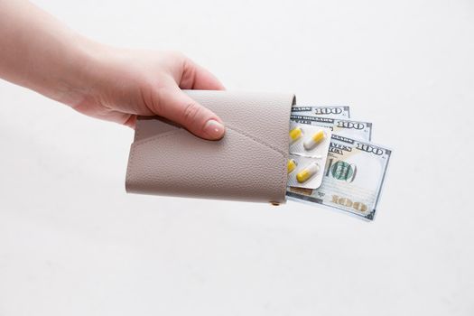 female hand holds a wallet with yellow capsule pills and dollar bills, white background