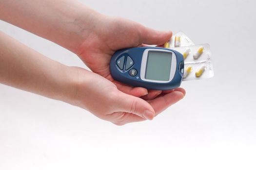 female hand holds a blue glucometer and several packs of tablets of capsules in long colors