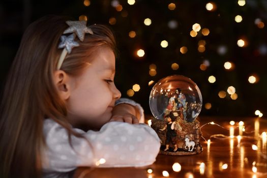 Girl looking at a glass ball with a scene of the birth of Jesus Christ near christmas tree