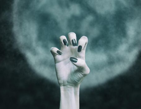 Scary hand with black nails of dead zombie man in front of full moon. Halloween concept.