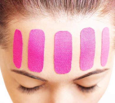 Beautiful woman with vertical kinesio tapes on her forehead against wrinkles, facelift beauty procedure.