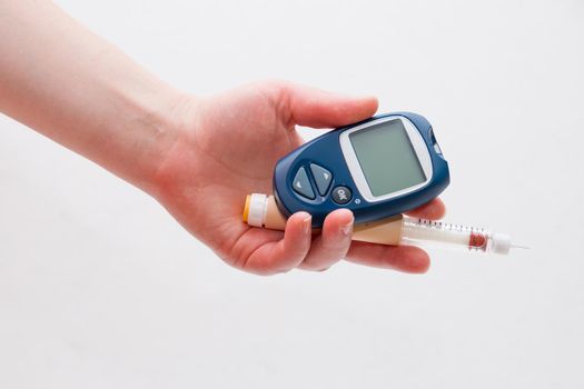 female hand holds a blue glucometer and a syringe for diabetes insulin injection pen