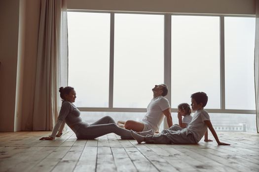 Fit parents are sitting on floor with daughter and son and having rest during training at home