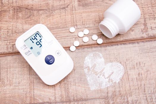 blood pressure monitor and white jar with tablets on a wooden background, heart made of white powder, pulse drawn, copy space, top view, heart pressure concept