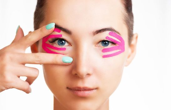 Front view portrait of smiling beautiful young woman with kinesiology tapes on eyelid against wrinkles, anti-aging beauty procedure.