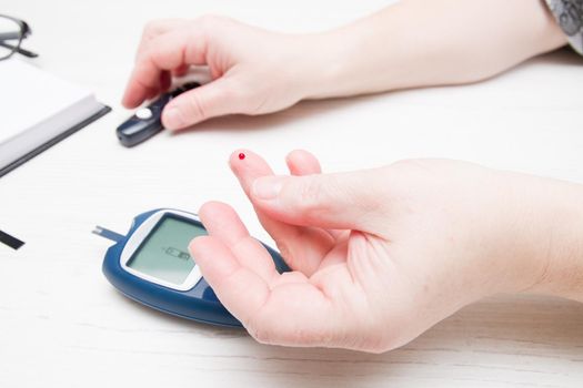 female hand with a drop of blood on a finger, measuring blood sugar, diabetes concept, glucose meter in the back