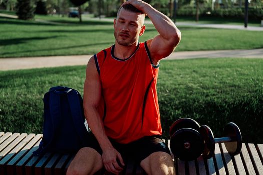 Cheerful male athlete in the park sits on a bench. High quality photo