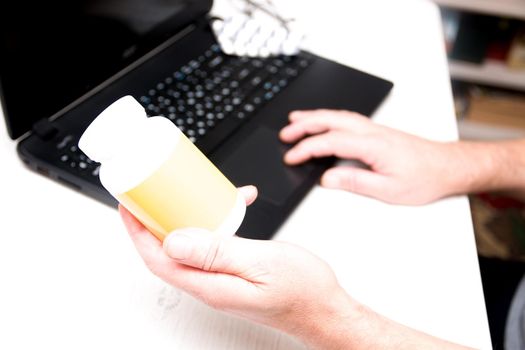 male hand holds a jar of medicine on a laptop background, online instinct, chat tips