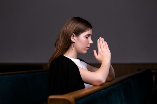 A Christian girl in white shirt is sitting and praying with humble heart in the church.