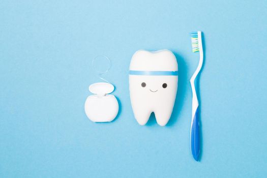 sweets, toothbrush, dental floss and toy tooth on a blue background, tooth model with a smile, protection of the oral cavity from caries concept, pediatric dentistry advertising