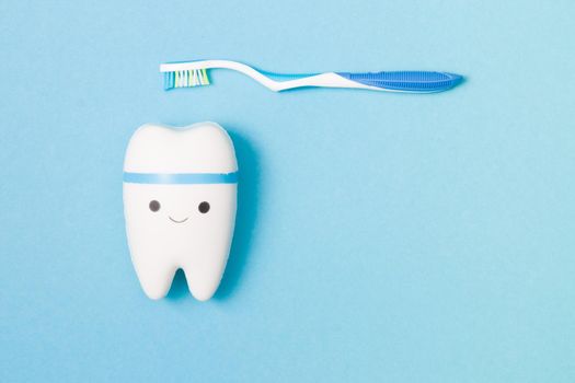 sweets, toothbrush, dental floss and toy tooth on a blue background, tooth model with a smile, protection of the oral cavity from caries concept, pediatric dentistry advertising