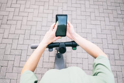 Woman using smartphone while standing with an electric scooter, mock-up. Point of view in first person.