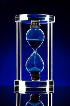 Hourglass illuminated on dark blue background close up photo