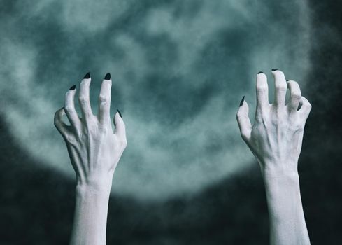 Terrible hands of a dead zombie man on background of full moon. Halloween and horror theme.