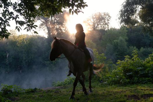 Young woman riding a horse on a beautiful landscape. Clear lake at morning fog. Sunrise Wide shot