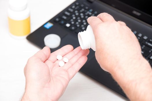 male hand pours medicine into a palm on a laptop background, online treatment concept, connection with a doctor