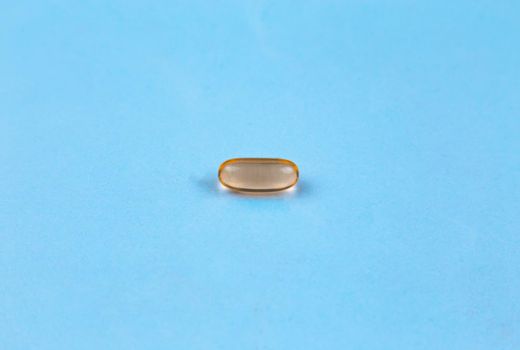 Fish oil supplement capsule isolated on blue background.