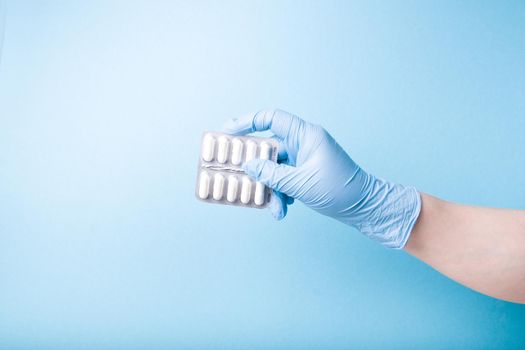 hand in a blue disposable medical glove holds a blister with white capsules blue background copy space