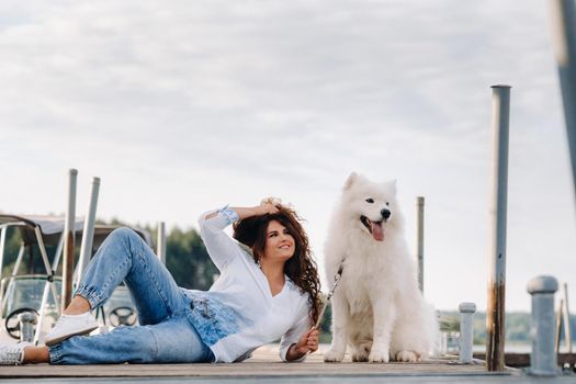 a happy woman with a big white dog lies on a pier near the sea at sunset.