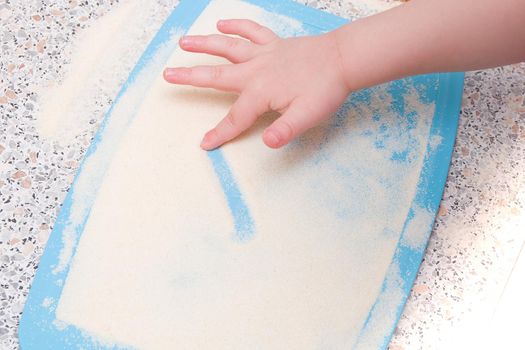 a small child draws a finger with semolina, a kitchen table, the development of fine motor skills, what to do with a child, cutting board blue