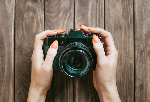 Unrecognizable woman holding vintage photo camera at wooden table. Point of view in first person.