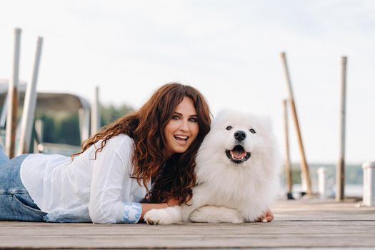 a happy woman with a big white dog lies on a pier near the sea at sunset.