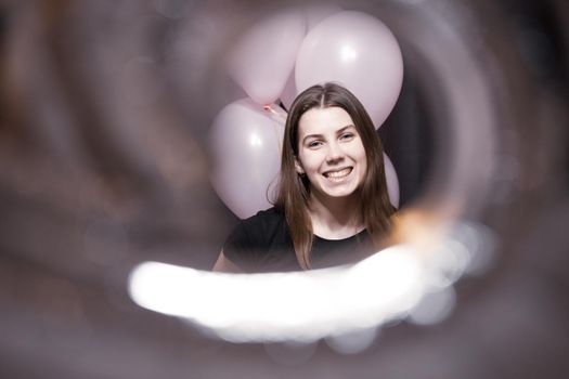 View through the tunnel. The face of a pretty girl with an emotion of joy that holds pink balloons on her birthday