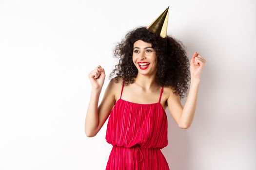 Happy birthday girl celebrating, wearing party hat and red dress, dancing and having fun, standing against white background.