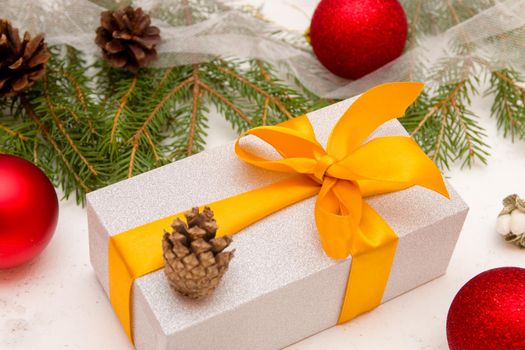 silver gift box with a gold ribbon bow, fir branches, cones and Christmas balls on the background, new year background