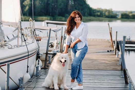 a happy woman with a big white dog stands on the pier near the yacht.
