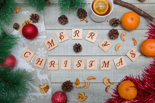 wooden boxes with the inscription Merry Christmas, pine branches, Christmas toys, tangerines, tea with lemon, Christmas mood, top view, wooden background