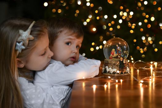 Children looking at a glass ball with a scene of the birth of Jesus Christ near christmas tree