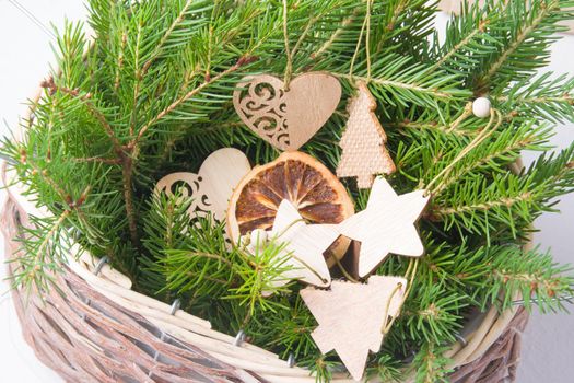 wooden eco friendly Christmas toys and fresh tree branches in a wicker basket on a white background, zero waste life style