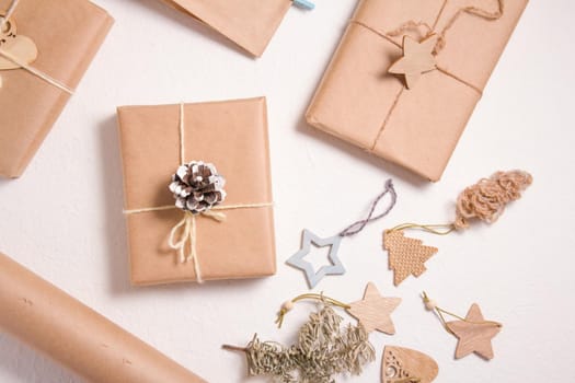 several gift wraps wrapped in kraft paper on a white background, eco friendly christmas concept, zero waste gifts, wooden christmas toys, a spruce branch and a pine cone on a white background