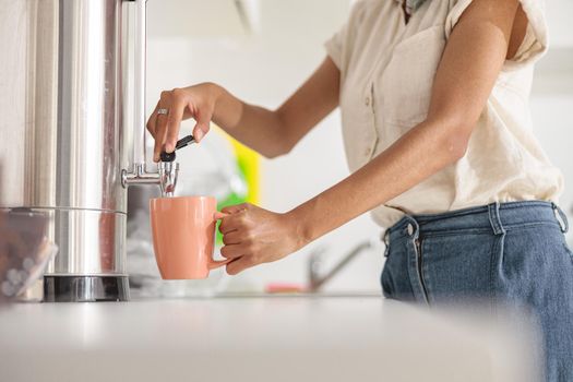 Close up of female hands holding cup while preparing hot drink on the kitchen