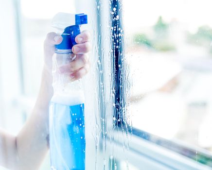 Woman hand holding bottle of blue cleaning spray, through transparent window