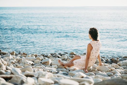 Beautiful young woman resting on pebble coast and enjoying view of sea