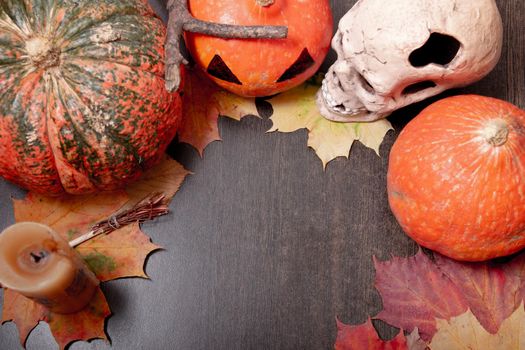 ceramic skull, candle, decorative broom and halloween pumpkins on a dark brown table background, autumn leaves and cones, copy space, top view