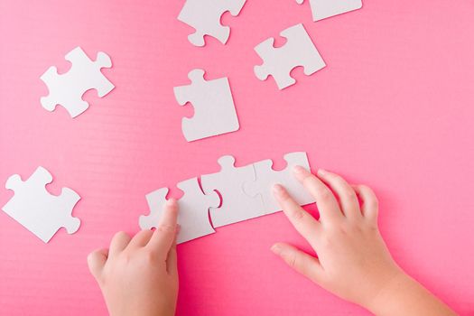 children's hands fold a paper white puzzle on a pink background development of fine motor skills of hands