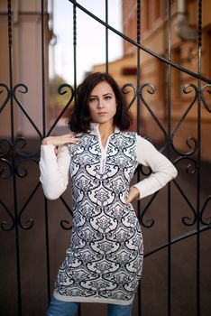 portrait of a young woman with black hair standing near the metall fence. Young woman modern portrait.