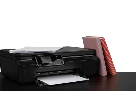 Printer and stack of books on black table against white background, close up