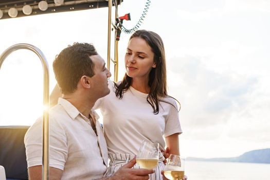 Young loving couple sitting on the yacht deck and drinking wine together