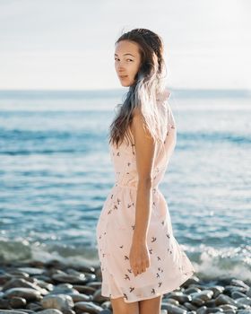 Beautiful young woman walking on pebble beach near the sea, looking at camera