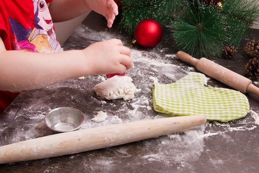 children hand makes cookies for Christmas, new year, wooden background, rolling pin on the table, dough in flour, copy place