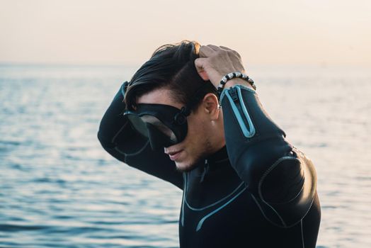 Diver young man putting on a mask on background of sea