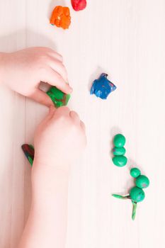 a small child sculpts a caterpillar from green plasticine on a wooden table, developing fine motor skills of hands, playing with a child at home, preparing for kindergarten, stay at home